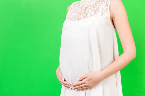 在绿色背景下靠近怀孕的腹部 妈妈穿着白色的衣服 紧紧抓住她的腹部 父母身份的概念 复制空间 — 图库照片