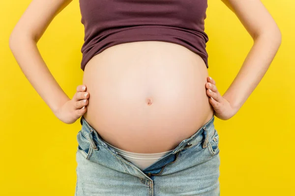妊娠中のお腹をコピースペースでカラフルな背景で閉じます オープンジーンズの未来の母親は彼女の裸の赤ちゃんのバンプを受け入れています 母性概念 — ストック写真