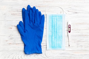 Tıbbi eldivenlerin üst görüntüsü, dijital termometre ve tahta arka planda fotokopi alanı olan cerrahi maske. Coronavirus karantina konsepti.
