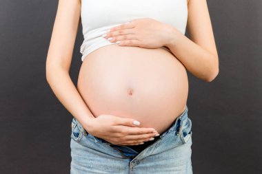 Fermuarsız kotlu hamile bir kadının renkli arka planda çıplak karnını fotokopi çekerken görüntüsü. Bebek bekleyen konsept.