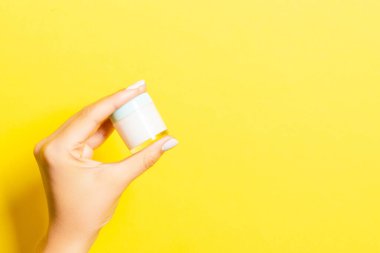 Kadının eli sarı arka planda bir kozmetik kavanozu tutuyor. Tasarımınız için fotokopi alanı var..