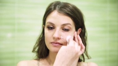 Kız yeşil banyodaki pamuk pedi kullanarak makyajı temizliyor.