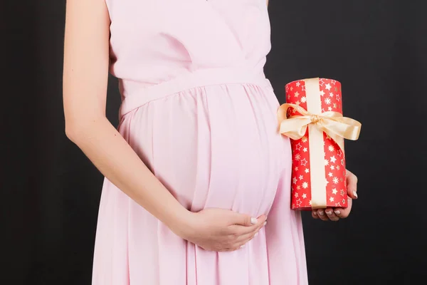 黒の背景にギフトボックスを保持ピンクのドレスで妊婦の肖像画を閉じます 妊娠祝いだ スペースのコピー — ストック写真