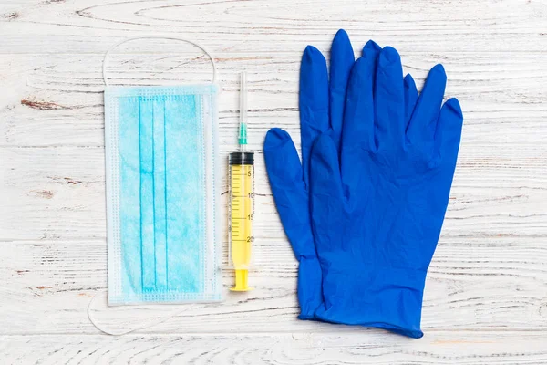 Top view of disposable surgical mask, pair of latex medical gloves and syringe on wooden background. Protect your health concept with copy space.