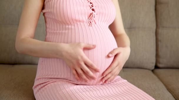 Detailní záběr těhotné ženy hladící její břicho na pohovce