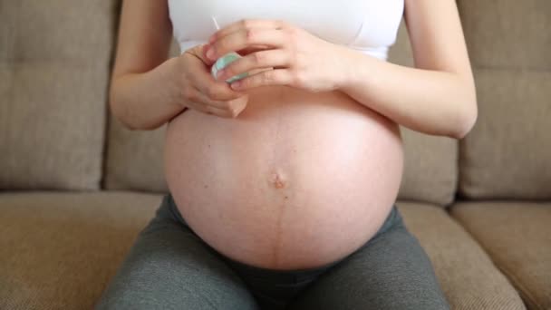 女人在家里的沙发上用奶油润滑怀孕的腹部 以达到伸展的效果 人体化妆品抗拉伸皮肤慢动作 — 图库视频影像
