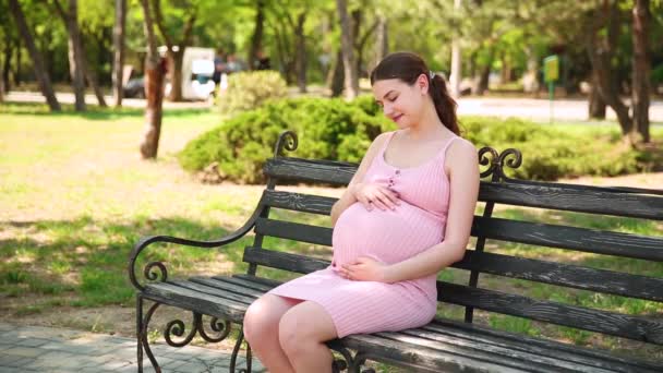 妊娠中の女の子が公園のベンチに座り胃が痛み始めます 妊娠中の女性は胃を撫でて触れ — ストック動画