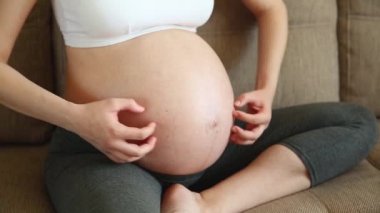 Karnını eliyle kaşıyan hamile bir kadın. Kızın midesi kaşınıyor ve çocuk karnına bastırıyor.