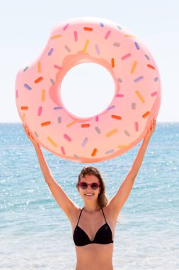 Güzel bir kadın plajda plajda plastik donut yüzüğüyle oynuyor..
