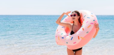 Donut şişirilebilir yüzüğün içindeki genç kadının portresi deniz arka planında birini arıyor. Kız sahilde birini bekliyor..