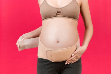 Hamile bir kadının arka planda çekilen acıya karşı hamilelik kemerini fotokopi çekerek kapatmasını istiyorum. Ortopedik abdominal destek kemeri kavramı.