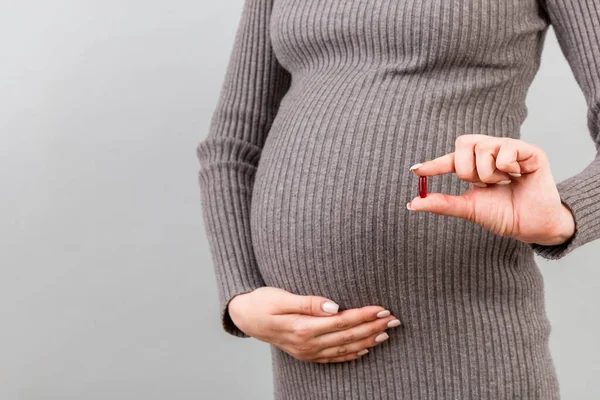 妊娠中の女性の閉じ込められます彼女の腹に対して彼女の手の中に薬を保持しますコピースペースとカラフルな背景で 妊娠中のビタミンを摂取する — ストック写真