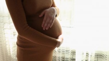 Hamile kadının ayakta karnını okşarken yakın plan fotoğrafı.