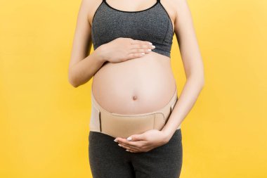 Esnek hamilelik bandajlı hamile kadının sarı arka plandaki ağrıyı yok etmek için fotokopi cihazını kapat. Ortopedik abdominal destek kemeri kavramı.