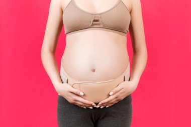 Pembe arka plandaki sırt ağrısını fotokopi aletiyle azaltmak için hamile kadına giydirilmiş elastik annelik bandını kapatın. Ortopedik abdominal destek kemeri kavramı.