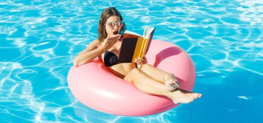 Genç bayan yüzme havuzundaki şişme yüzüğün üzerinde oturan bir kitap okuyor. Yaz rahatlama kavramı .