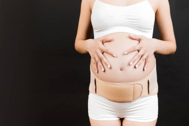 Siyah arka planda, fotokopi alanı olan iç çamaşırlı hamile bir kadının destekleyici görüntüsü. Ortopedik abdominal destek kemeri kavramı.