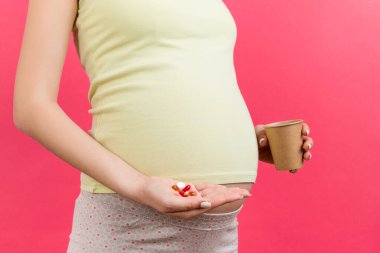 Bir elinde bir bardak su, diğer elinde de renkli arka planda fotokopi alanı olan bir yığın hap tutan hamile kadına yakın durun. Hamilelik sırasında ilaç almak.