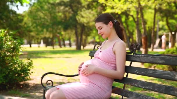 一个怀孕的女孩坐在公园的长椅上 她的胃开始疼痛 她开始正常呼吸 怀孕妇女摸肚子 — 图库视频影像