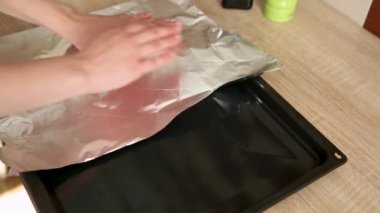 Kadın eli folyoyu sarar, bir parça keser ve pişirmede kullanmak üzere bir yemek tepsisine uzanır..