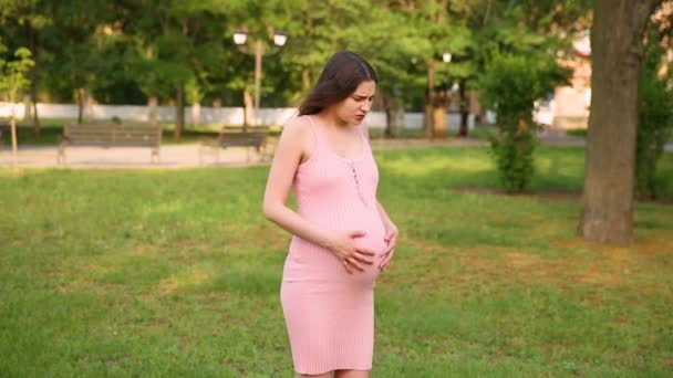 妊娠中の女の子が公園に立っていると 彼女の胃が痛み始めます 妊娠中の女性が胃を撫でて横から横に歩き — ストック動画