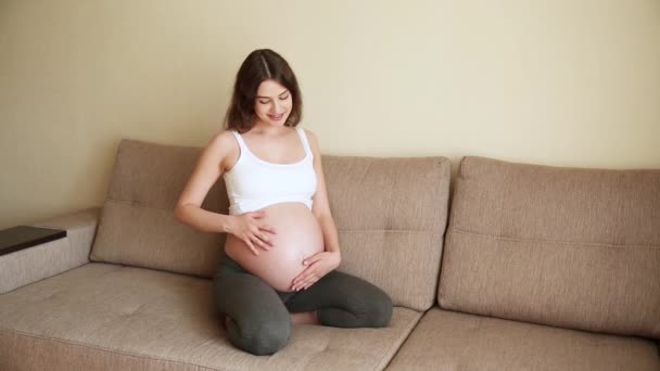 怀孕的概念 漂亮的已婚孕妇揉着肚子和孩子说话 夏日快乐的未来母亲坐在沙发上 — 图库视频影像