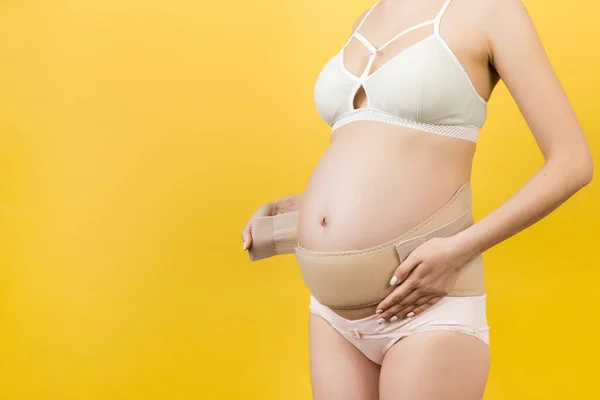 用内衣裤包扎孕妇的形象 以减少背痛的黄色背景与复印空间 整形外科腹部支持带概念 — 图库照片