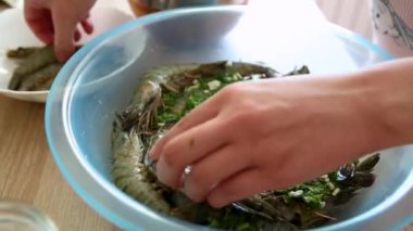 Terbiye edilmiş karides. Kadın elleri ev mutfağındaki bir kasede çiğ karides turşusu kurar. Yakın plan.