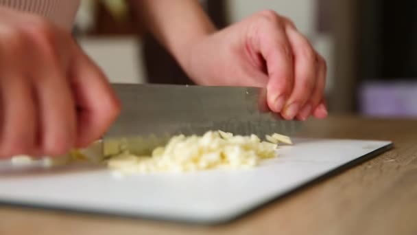 女の子は板にナイフでニンニクを切る 台所の女性はニンニクの皮をむいた — ストック動画
