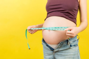 Annemin fermuarsız kotla hamile karnını renkli bir mezurayla ölçerken çekilmiş görüntüsü. İnç Ölçümü.