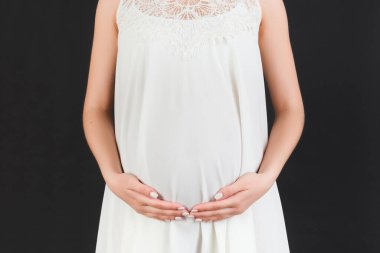 Siyah arka planda karnını tutan beyaz elbiseli hamile bir kadın resmi. Müstakbel anne bebeğini bekliyor. Boşluğu kopyala.