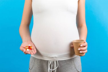 Bir elinde bir bardak su, diğer elinde de renkli arka planda fotokopi alanı olan bir yığın hap tutan hamile kadına yakın durun. Hamilelik sırasında ilaç almak.