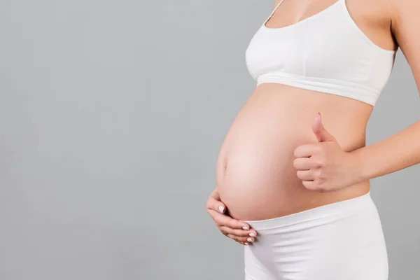 白い下着姿の妊婦の豊満なショットは 灰色の背景で彼女の赤ちゃんのバンプの上にクールなジェスチャーを表示します 幸せな妊産婦 スペースのコピー — ストック写真