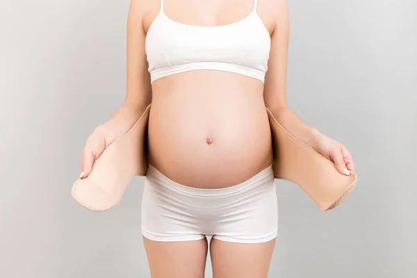 Крупный План Беременной Женщины Белых Трусах Надевающей Повязку Сером Фоне — стоковое фото