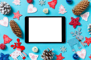 Yeni yıl oyuncakları ve mavi arka planda süslemelerle çevrili dijital tabletin üst görüntüsü. Noel zamanı konsepti.
