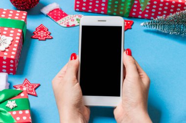 Neşeli mavi arka planda kadın elinin telefonunun üst görüntüsü. Noel süsleri. Yeni yıl tatili. Model.