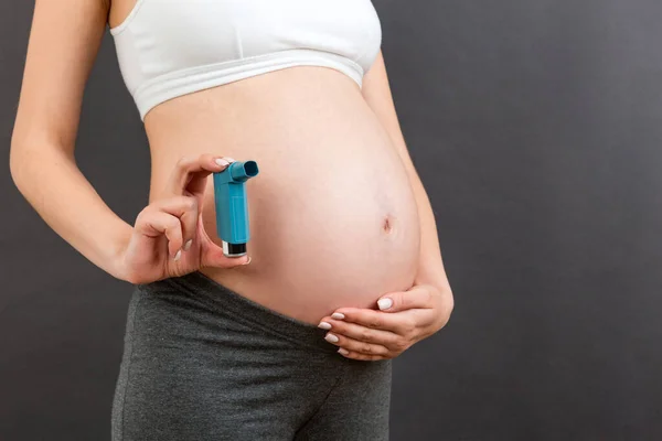 Close up of pregnant woman using asthma inhaler during attack for being healthy at colorful background with copy space. Health care concept.