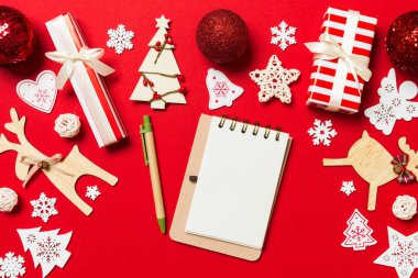 Kırmızı arkaplanda Noel süslemelerinden yapılmış defterin üst görüntüsü. Yeni yıl konsepti.