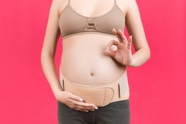 Hamile bir kadının sırt ağrısına karşı ortopedik bandajı destekleyin. Pembe arka planda fotokopi aletiyle sorun olmadığını gösterin. Ortopedik abdominal destek kemeri kavramı.