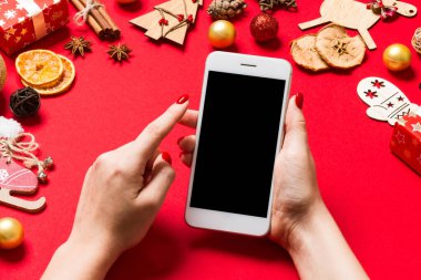 Kırmızı arka planda bayanların telefonunun üst görüntüsü. Noel süsleri. Yeni yıl tatili. Model.