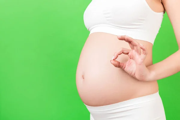 緑色の背景でお腹に対して大丈夫なジェスチャーを示す白い下着姿の正妊娠中の女性のトリミングされたイメージ 簡単で幸せな妊娠 スペースのコピー — ストック写真