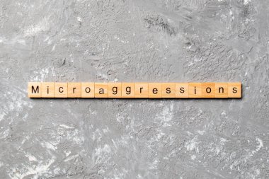 Microaggressions word written on wood block. Microaggressions text on cement table for your desing, concept. clipart