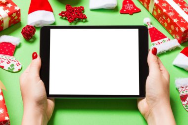 Elinde tabletle Noel süslemelerinden yapılmış yeşil arka planda gezen kadının üst görüntüsü. Yeni yıl tatili konsepti. Model.
