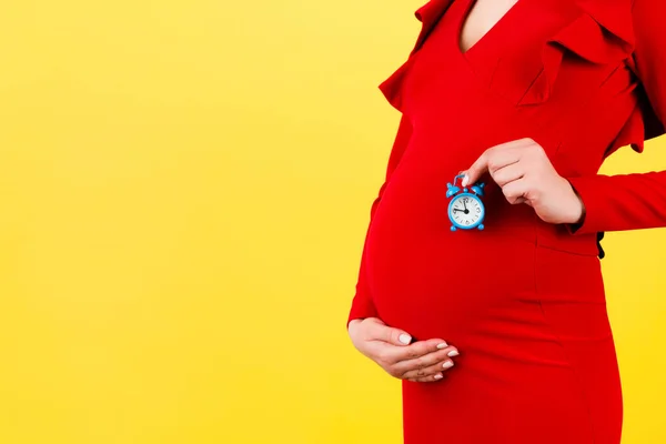Imagen Recortada Mujer Embarazada Vestido Rojo Sosteniendo Reloj Despertador Contra — Foto de Stock