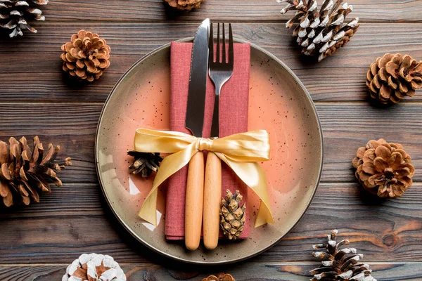 New Year set of plate and utensil on wooden background. Top view of holiday dinner decorated with pine cones. Christmas time concept.