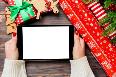Kadın ellerinin, köknar ağacı ve şenlikli süslemelerden yapılmış ahşap Noel arka planında bir tablet taşıdığı en üst görüntü. Yeni yıl tatili konsepti. Model.