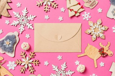 Tatil süsleri ve oyuncaklardan yapılmış pembe arka plandaki el sanatları zarfının en üst görüntüsü. Noel süsü konsepti.
