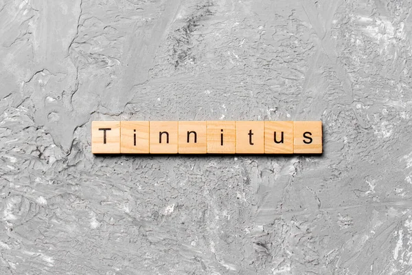 Tahta bloğa yazılmış bir kelime. Çimento sehpası üzerindeki TINNITUS metin desing, konsept.