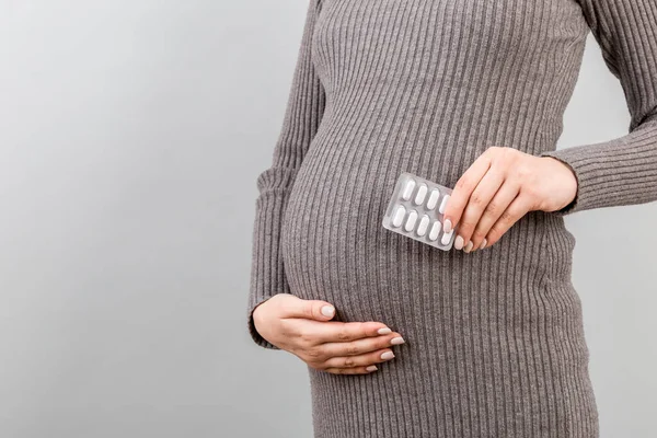 妊娠中の女性がコピースペースでカラフルな背景で腹に薬のブリスターを保持しているイメージを切り取った 栄養補助食品の概念 — ストック写真