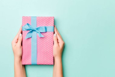 Kadın elleri renkli kağıda sarılı Noel veya diğer tatil hediyelerini verir. Hediye kutusu, hediye süslemesi mavi masada, üst görünümde kopya alanı.